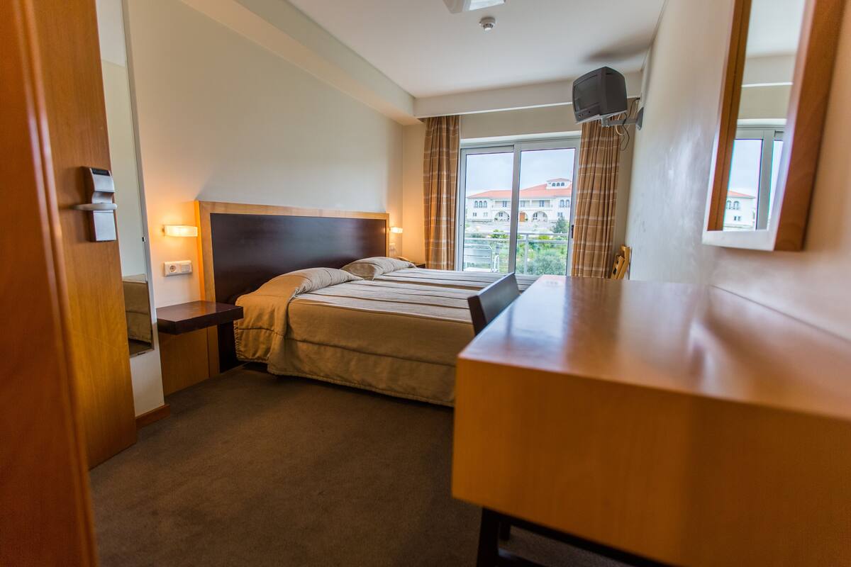 Una habitación de hotel con cama, mesitas de noche, un escritorio y una ventana con cortinas.