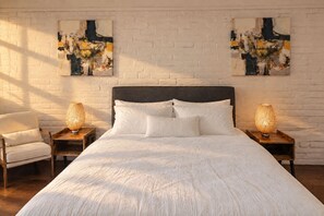 Une chambre à coucher avec un grand lit, deux tables de chevet, une chaise et des tableaux abstraits accrochés au mur.