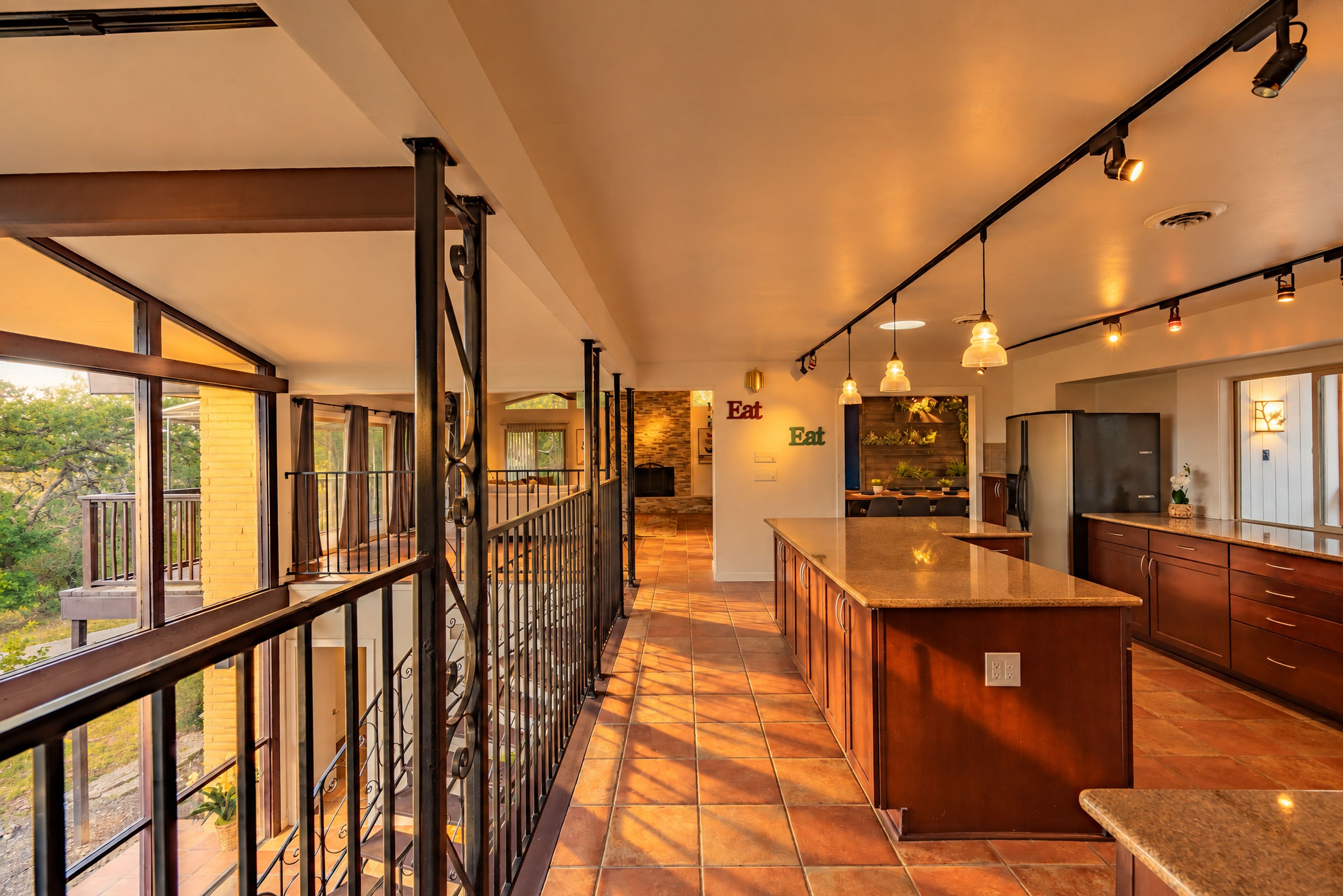 A modern kitchen with a large island, pendant lighting, and a view through a glass railing.