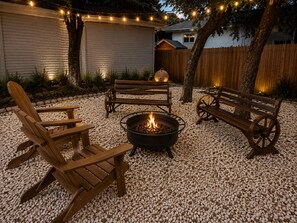 Un espace extérieur aménagé avec des bancs en bois et un foyer entouré de galets.
