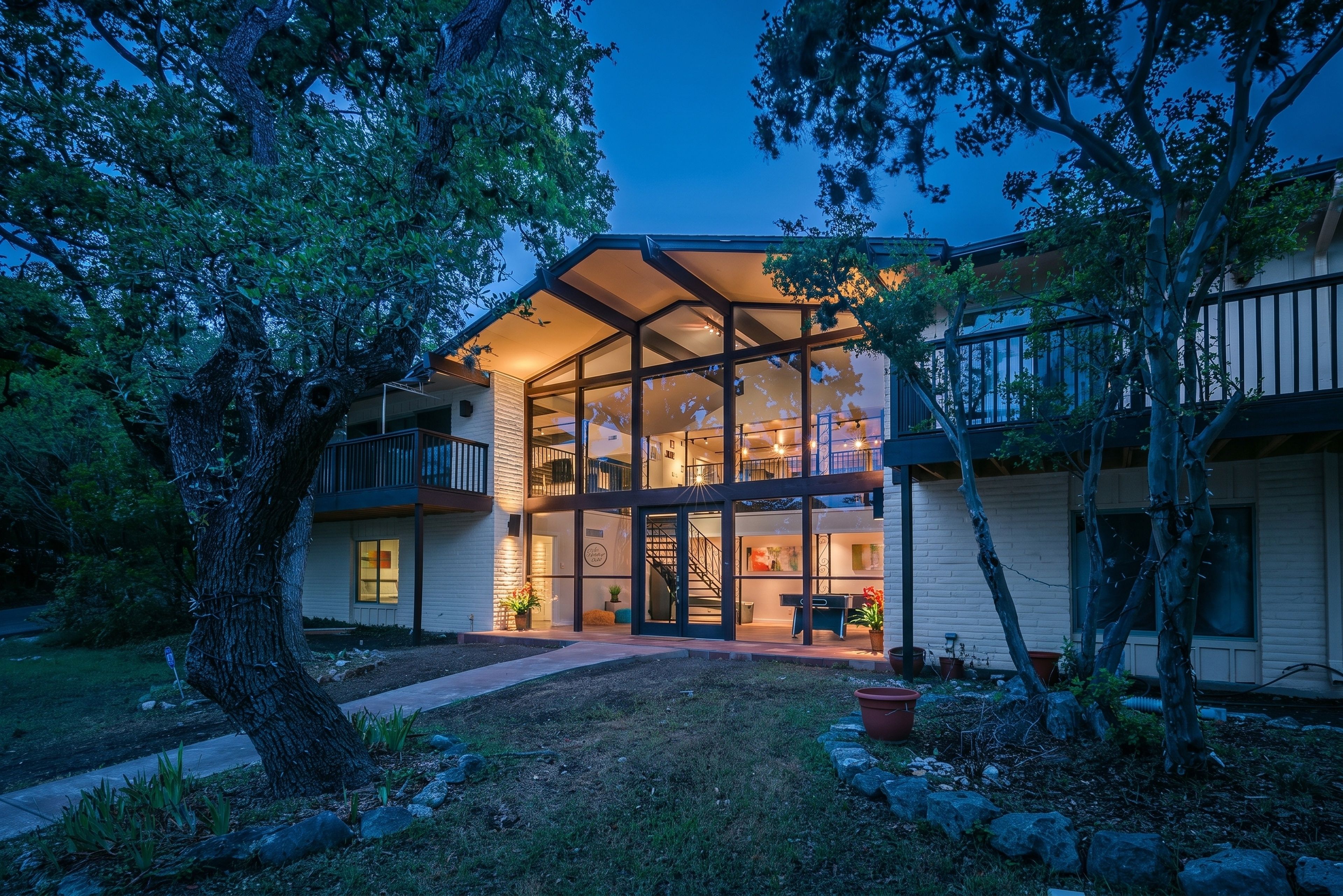 Une maison à deux étages avec une façade en verre, un balcon et une pelouse bien entretenue.