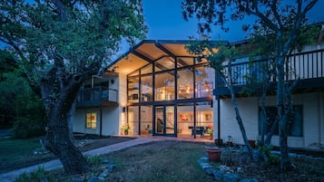 Une maison à deux étages avec une façade en verre, un balcon et une pelouse bien entretenue.