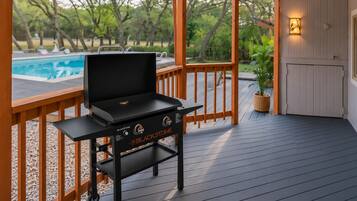 A Blackstone grill on a wooden deck with a pool in the background.
