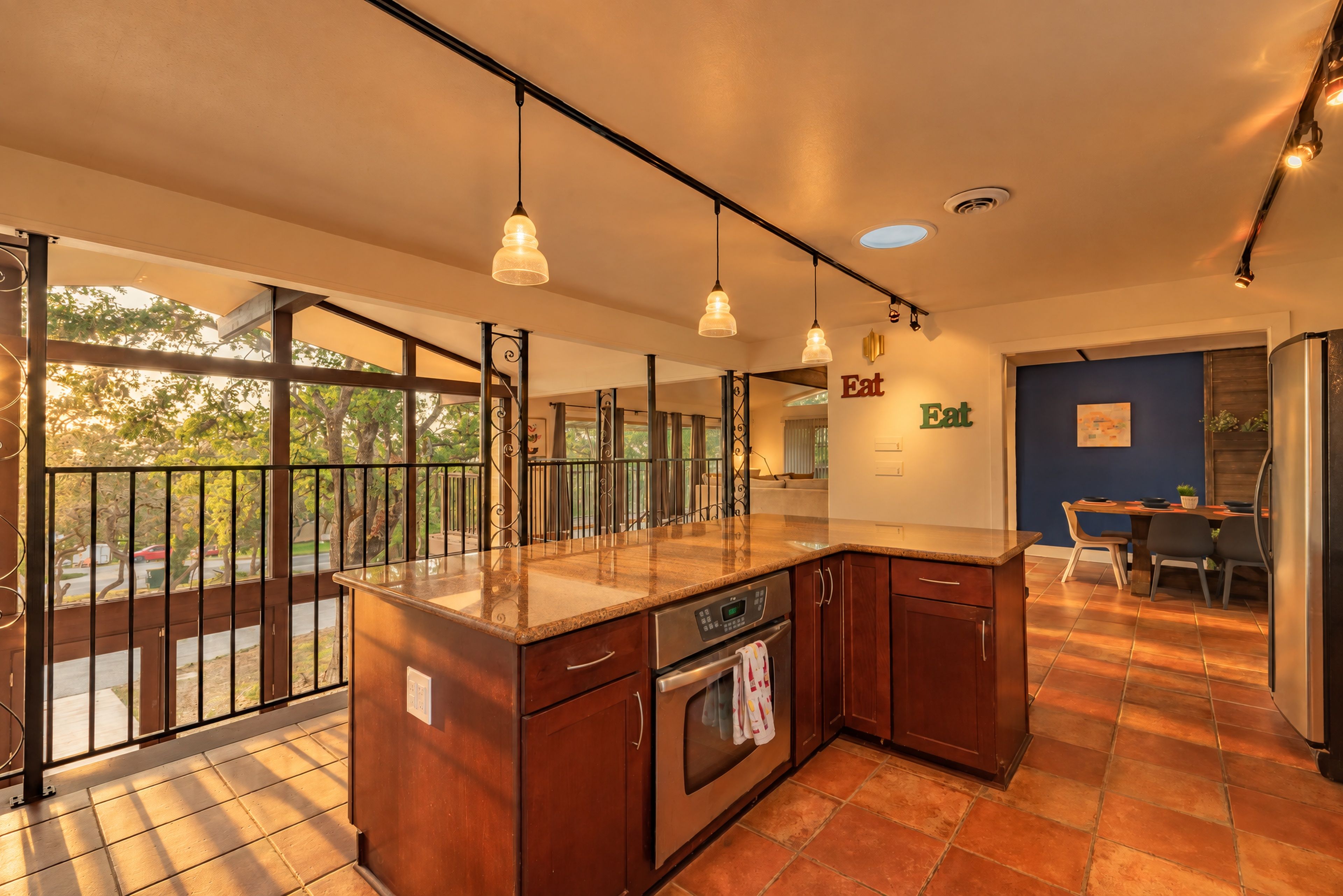 A modern kitchen with a large island, pendant lighting, and a view through large windows.