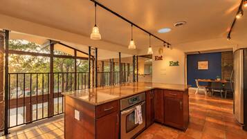 A modern kitchen with a large island, pendant lighting, and a view through large windows.
