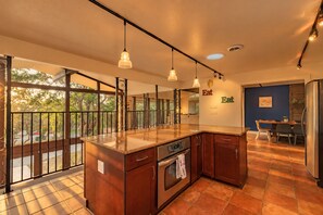 A modern kitchen with a large island, pendant lighting, and a view through large windows.