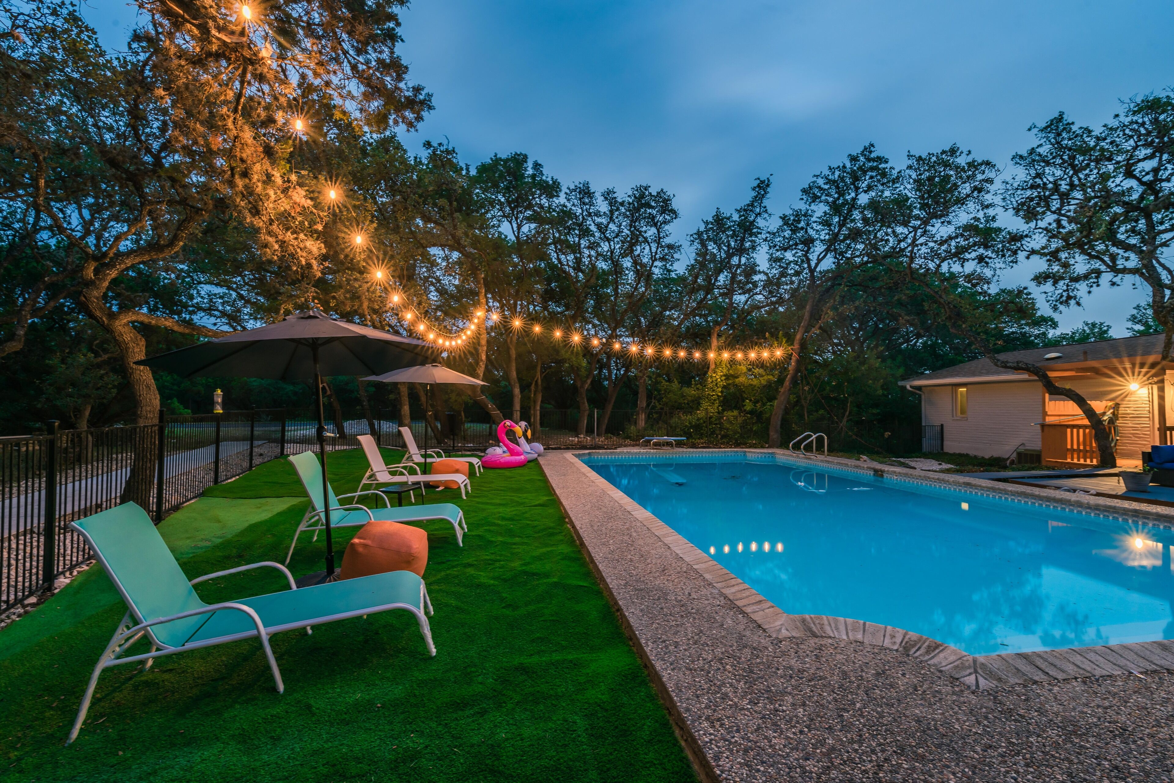 A swimming pool with lounge chairs and umbrellas, surrounded by trees and string lights.