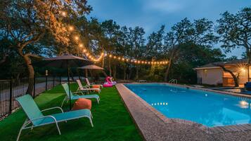 A swimming pool with lounge chairs and umbrellas, surrounded by trees and string lights.