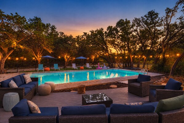 A swimming pool with lounge chairs and umbrellas, surrounded by trees and string lights.