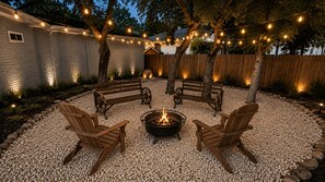A circular seating area with a fire pit, surrounded by wooden chairs and benches, under string lights.
