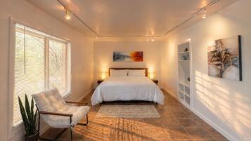 A bedroom with a bed, bedside lamps, a chair, a potted plant, and artwork on the walls.