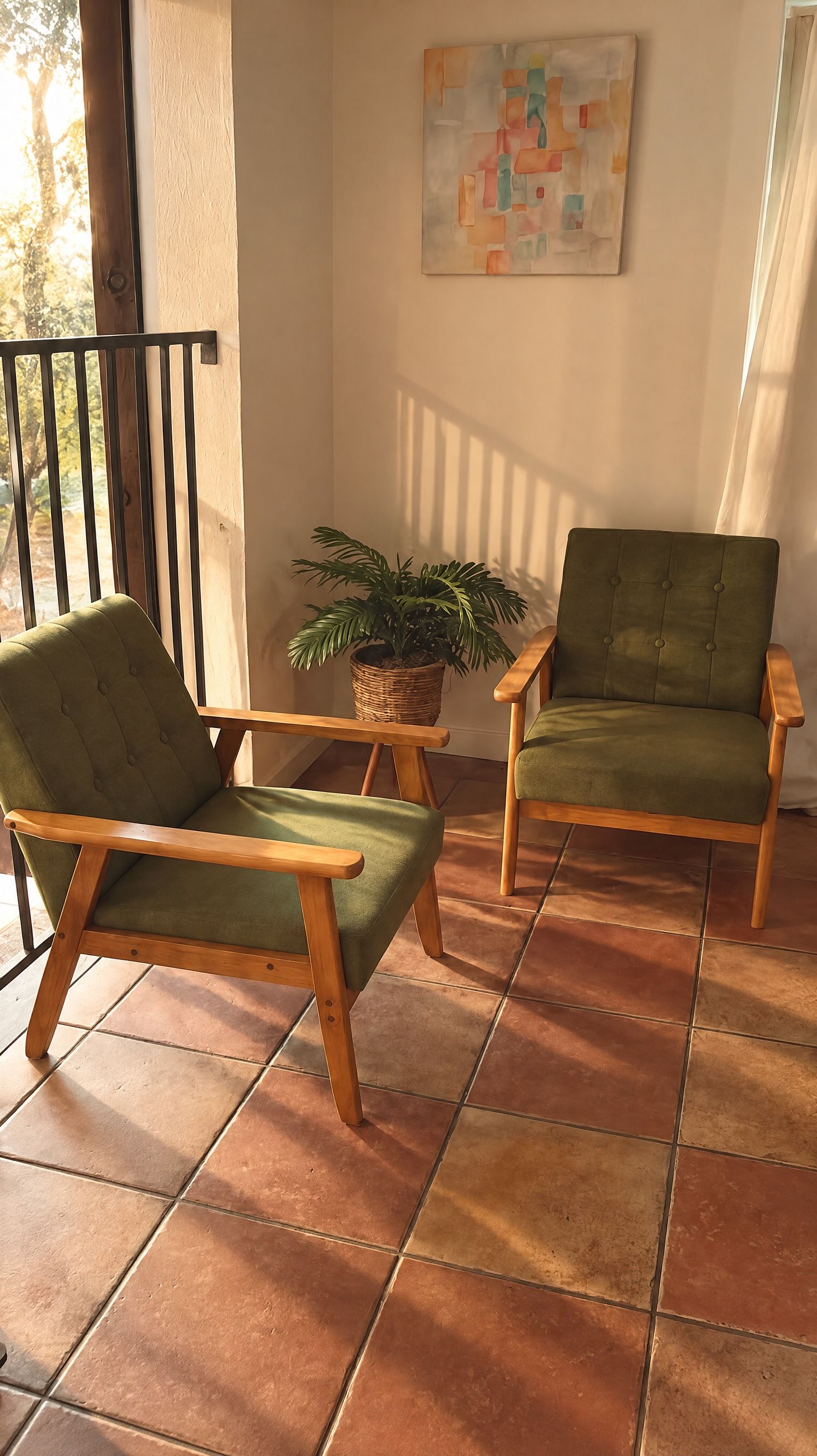 Ein Balkon mit zwei grünen Polsterstühlen, einem Topfpflanzen und einem Bild an der Wand.
