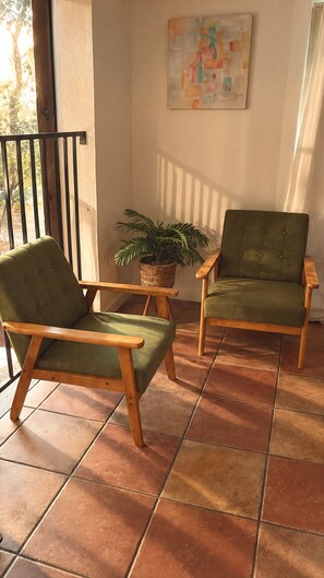 Un balcon avec deux fauteuils à revêtement vert, une plante en pot et un tableau accroché au mur.