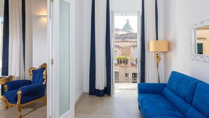 Une pièce avec un canapé bleu, un fauteuil bleu, une lampe et une vue sur un bâtiment coiffé d’un dôme, visible à travers une porte.