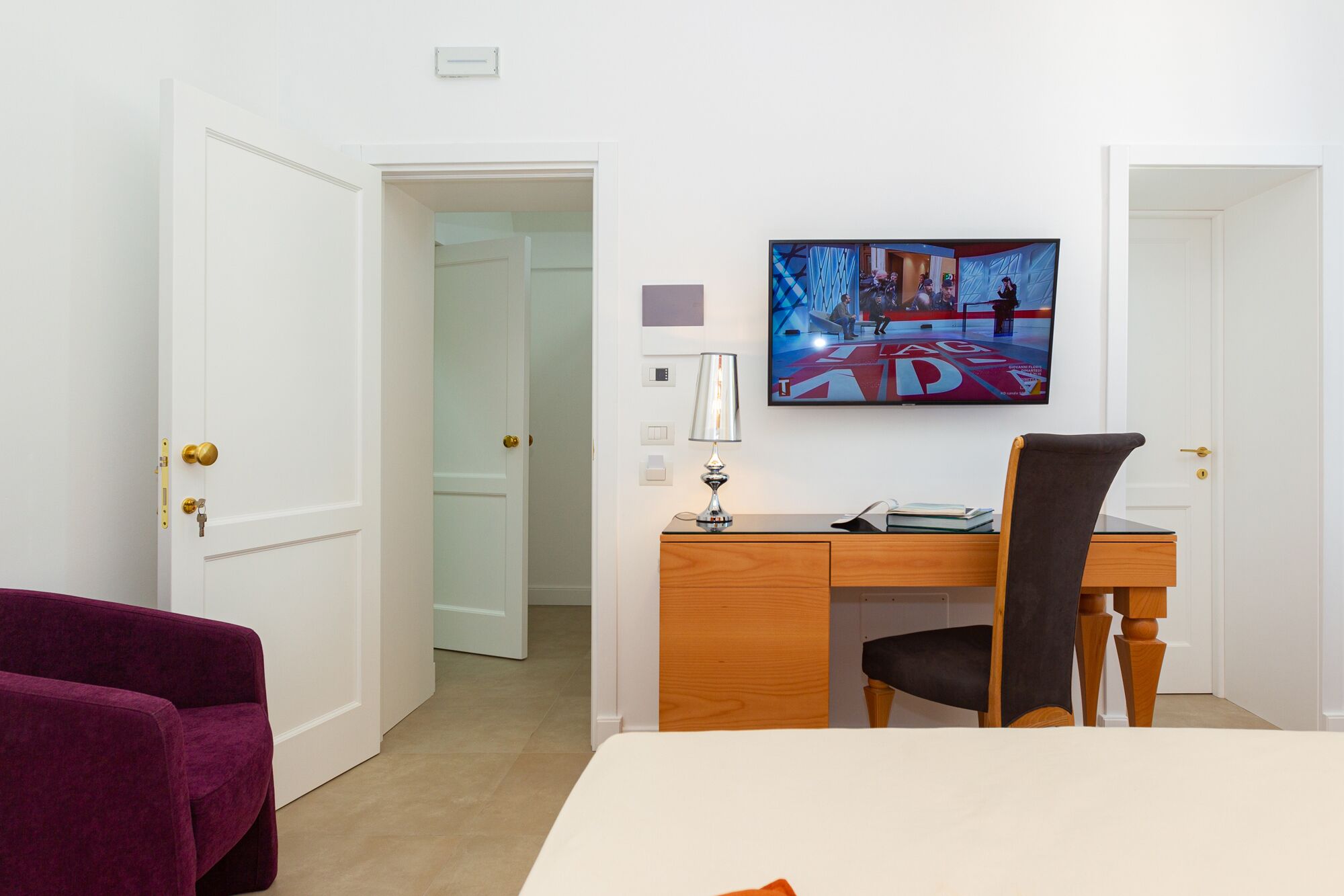 A hotel room with a bed, a desk with a chair, a television, and a door leading to another room.