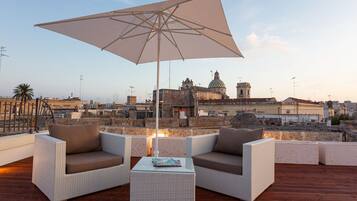 A rooftop terrace with wicker furniture, a table, and an umbrella.