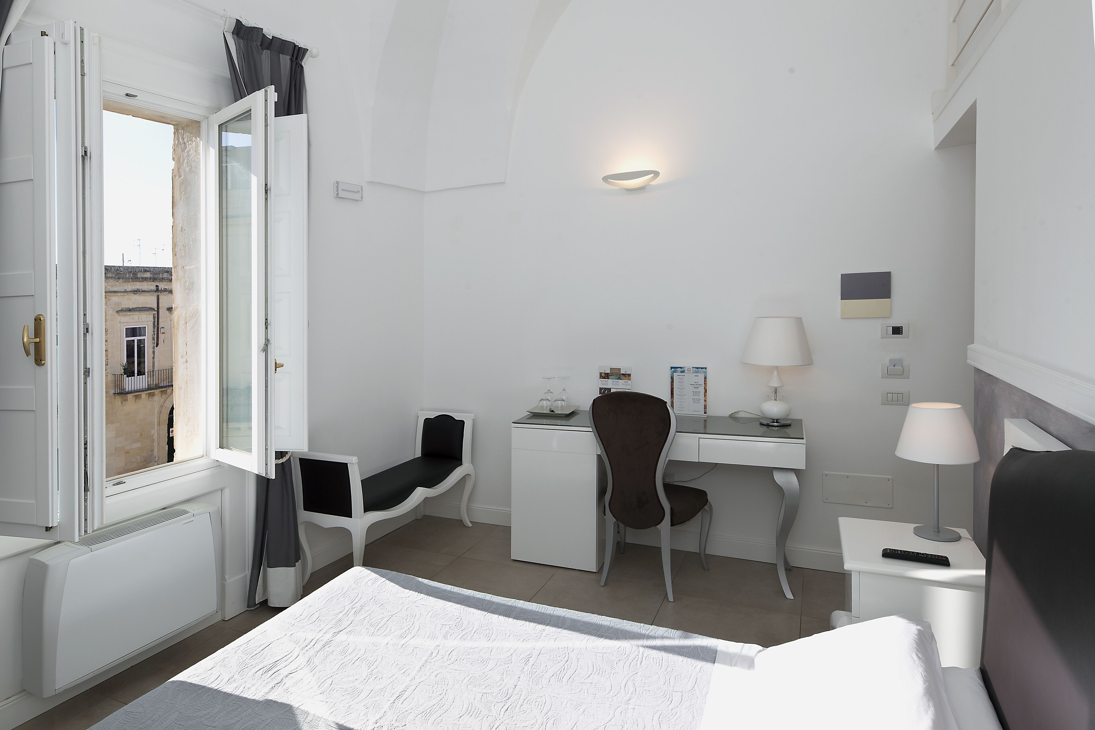 Habitación de hotel con cama, escritorio, silla, lámpara de escritorio, mesita de noche y ventana con cortinas.