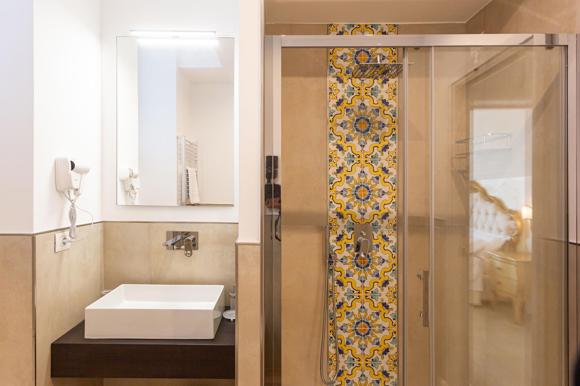 A bathroom with a white sink, a mirror, a towel rack, and a shower with decorative tiles.