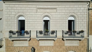 Une façade d’immeuble ornée de trois fenêtres en arc de cercle, d’une plaque portant l’inscription « PALAZZO MARINI » et d’éléments décoratifs disposés autour des fenêtres.