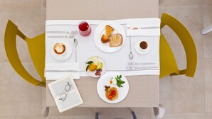 Une table mise pour le petit-déjeuner, avec un livre, des lunettes et différents plats.