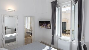 Une chambre avec un grand lit, un miroir, une fenêtre avec des rideaux et une vue sur l’extérieur.