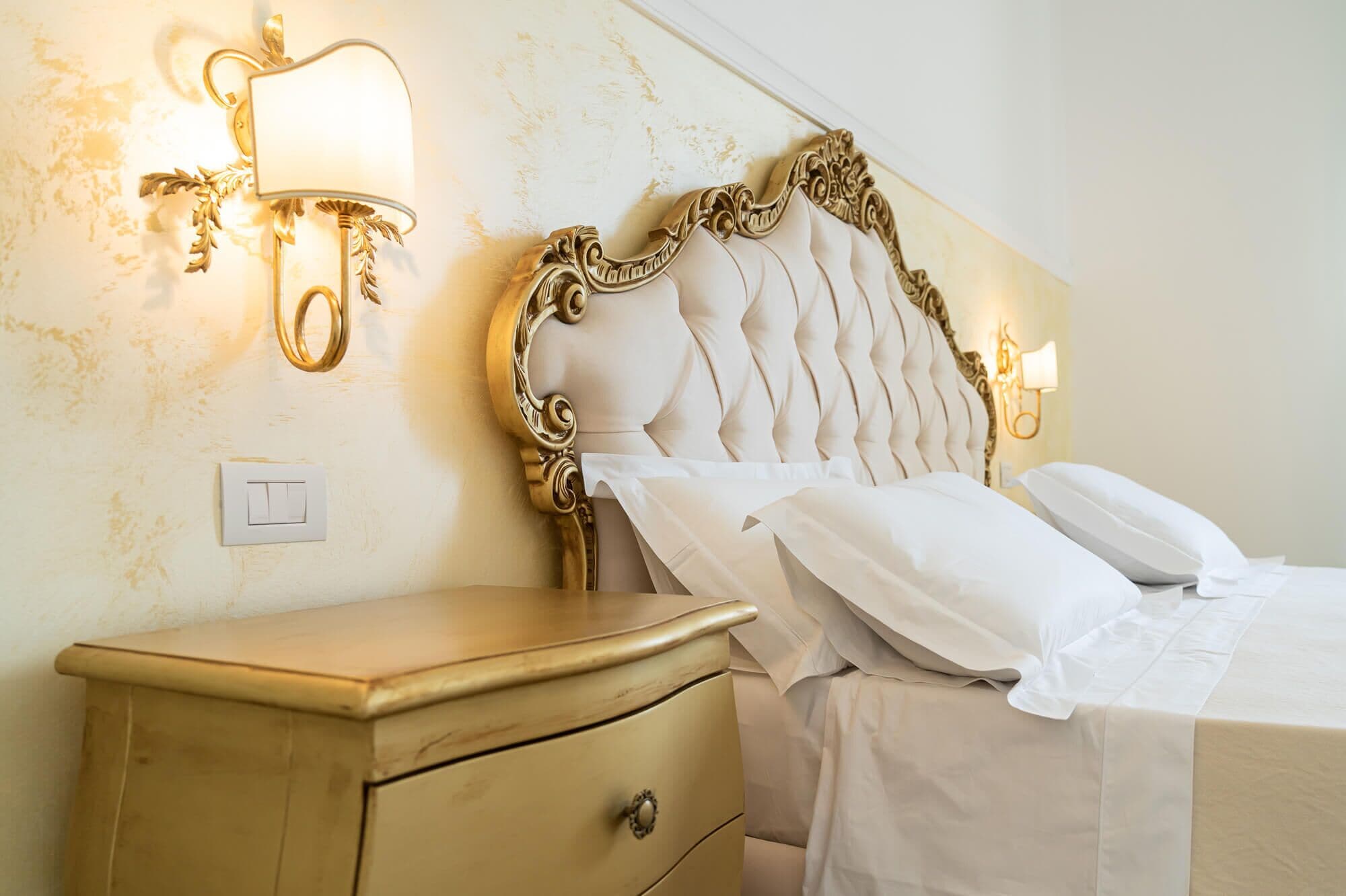 A bedroom with a classic design, featuring a tufted headboard, a bedside table, and wall-mounted lamps.