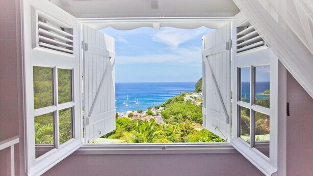 A room with a large window overlooking a coastal view, including the ocean and greenery. - "O Coeur de Deshaies" (Deshaies)