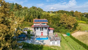 Ein zweistöckiges Haus mit Swimmingpool, umgeben von Bäumen und einer hügeligen Landschaft.