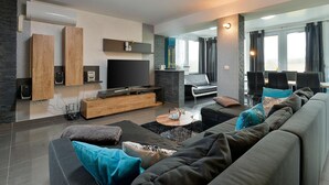 Ein modernes Wohnzimmer mit einem großen Flachbildfernseher, einer Holzunterhaltungsecke, einer Couch mit vielen Kissen und einem Essbereich mit Tisch und Stühlen.