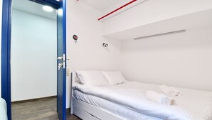 A single-bed room with a wooden floor, white walls, a blue door, and a white bed with rolled towels. - SOLO Apartment 1BR Apartment (Tbilisi)