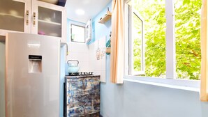 A compact kitchen with a refrigerator, a small stove, and a window with a view of greenery. - SOLO Apartment 1BR Apartment (Tbilisi)