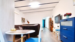 A modern living room with a brown leather sofa, a round table, and blue chairs. There is a TV and a blue cabinet in the room. - SOLO Apartment 1BR Apartment (Tbilisi)