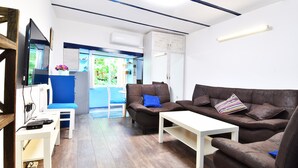 A modern living room with a brown leather sofa, a white coffee table, and a blue chair. There is a television on a wooden stand, and a white cabinet against the wall. - SOLO Apartment 1BR Apartment (Tbilisi)