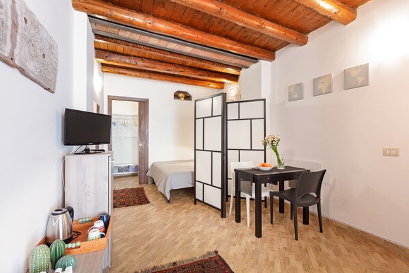 Quarto compacto com cama, televisão, mesa de jantar e cadeiras, e uma divisória.