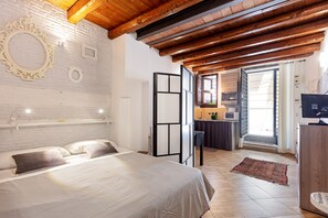 Quarto com cama, espelho, pequena cozinha e vista para o exterior.