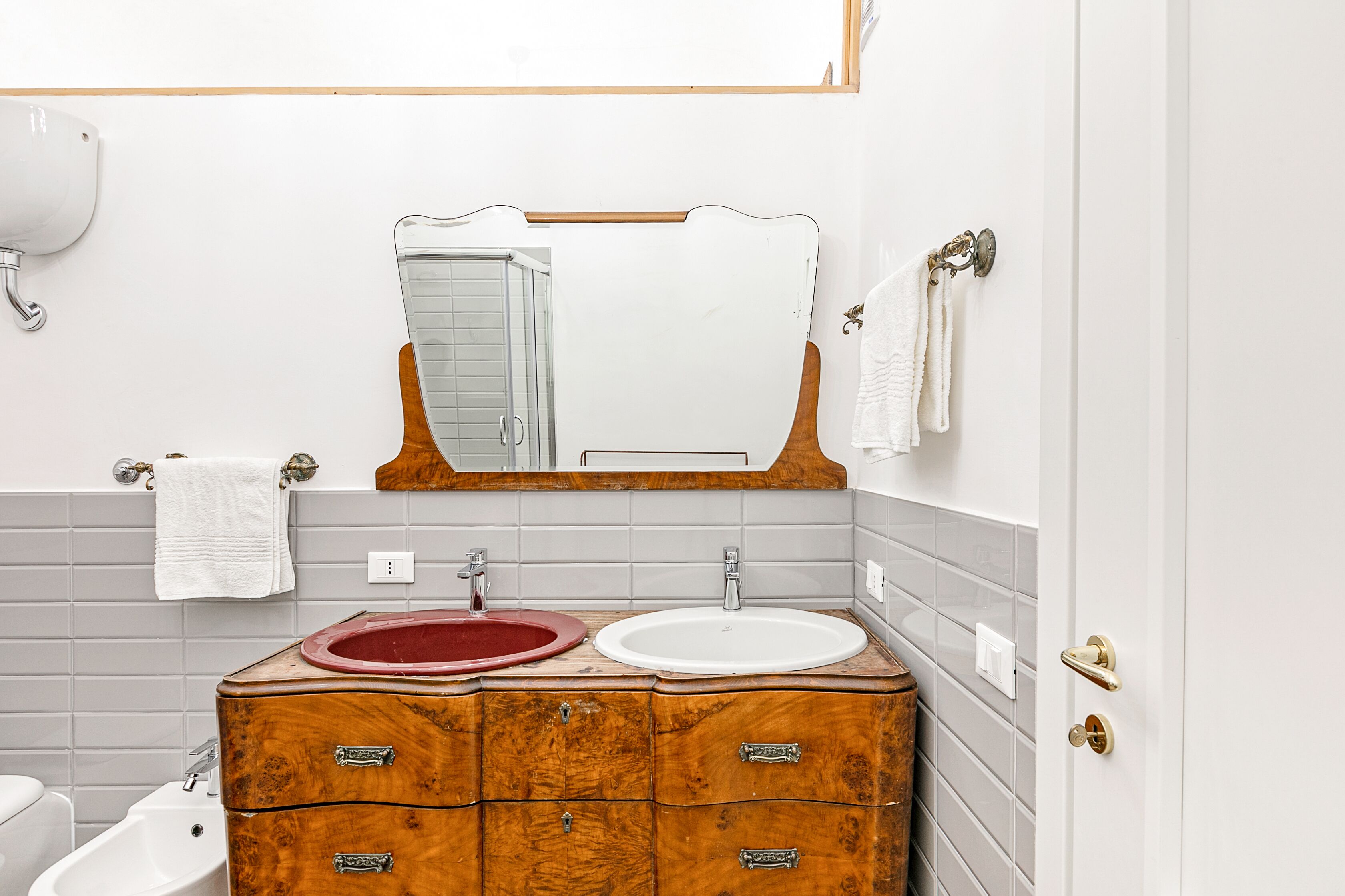Une salle de bain avec un meuble-lavabo en bois, deux vasques, un miroir et des toilettes.