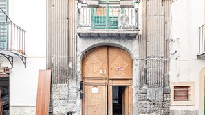 A historic building with a large wooden door, a balcony with a metal railing, and a small window on the right side. - Palazzo dei Normanni Stylish Apartment (Palermo)