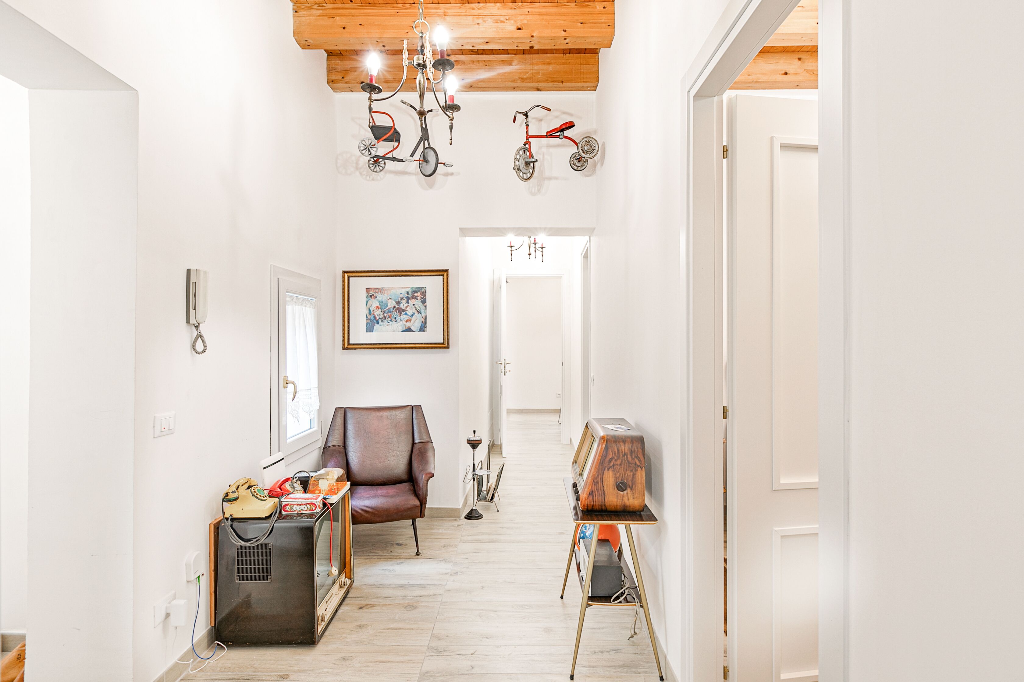 A narrow hallway with a wooden ceiling, a red tricycle, a vintage radio, and a framed picture on the wall.