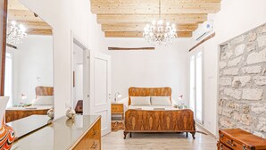 A bedroom with a wooden bed, a dresser, a mirror, and a stone wall. - Palazzo dei Normanni Stylish Apartment (Palermo)