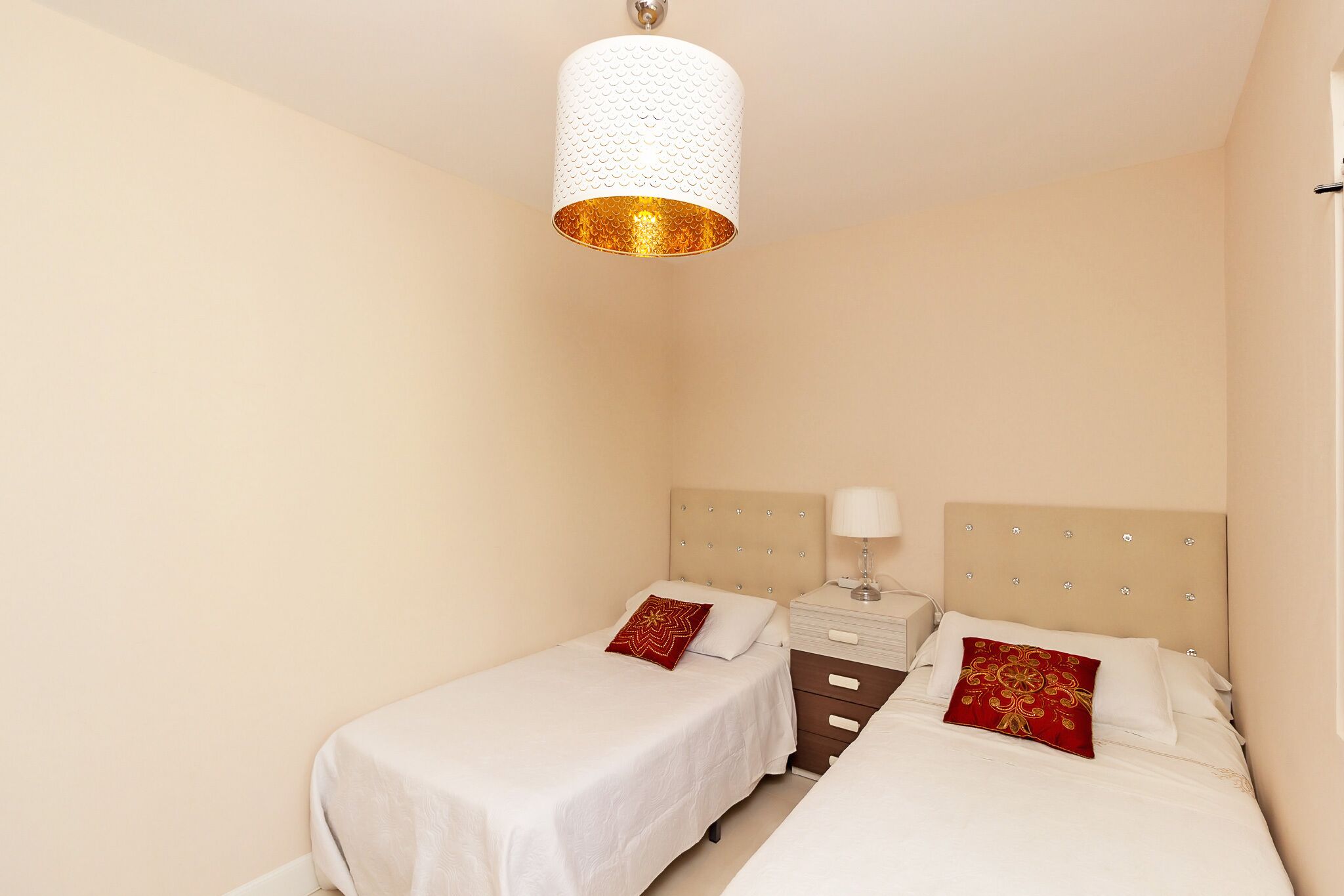 A bedroom with two beds, a nightstand, a lamp, and a textured ceiling light fixture.