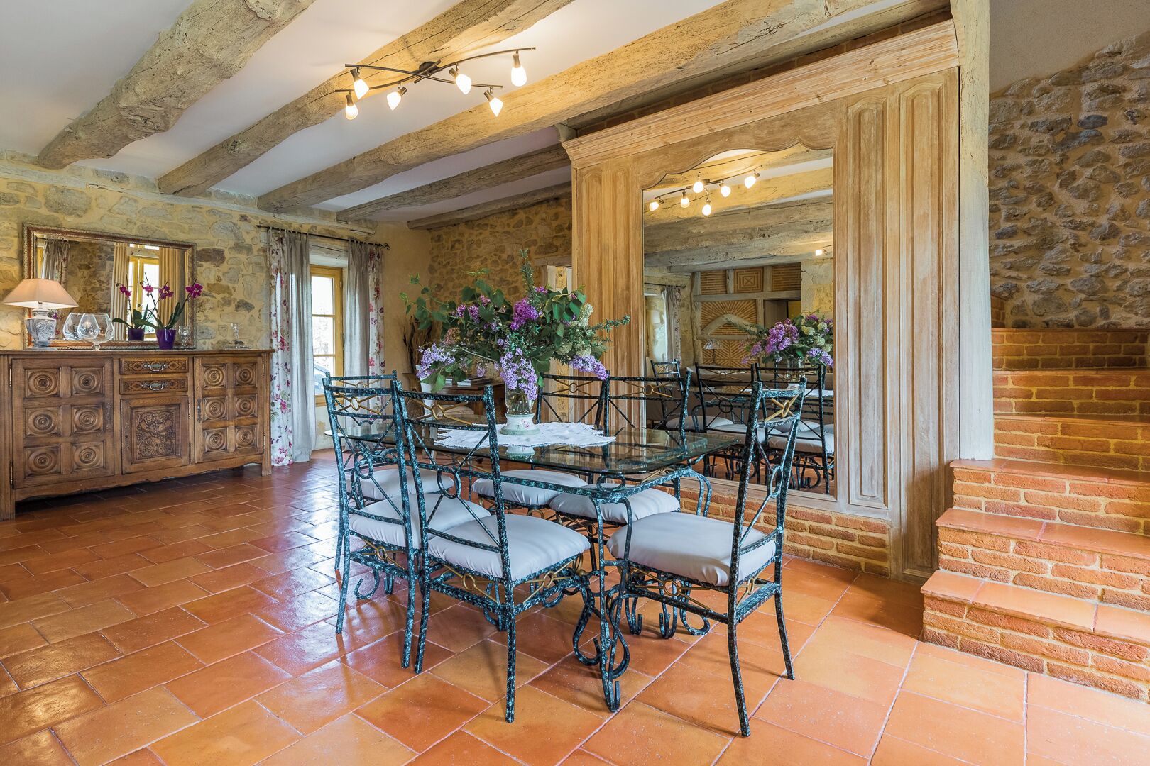 A dining area with a rustic stone wall, a wooden cabinet with glass doors, and a table set with chairs.
