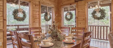A wooden cabin dining area with a table set for four, surrounded by chairs, and decorated with Christmas wreaths.