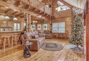 A cozy log cabin interior with a living room, kitchen, and dining area, featuring wooden floors, a fireplace, and a Christmas tree. - Luxury! 2 Master Suites w/Fireplaces|Game Room (SEVIERVILLE)