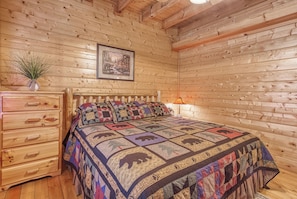 A wooden cabin bedroom with a bed, a dresser, a lamp, and a framed picture on the wall. - Luxury! 2 Master Suites w/Fireplaces|Game Room (SEVIERVILLE)