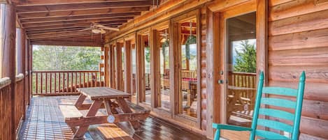 A wooden deck with a picnic table and chairs, a ceiling fan, and large windows.