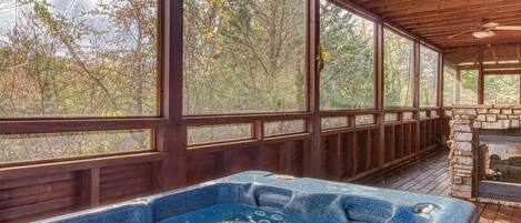 A wooden deck with a hot tub, large windows, and a stone fireplace.