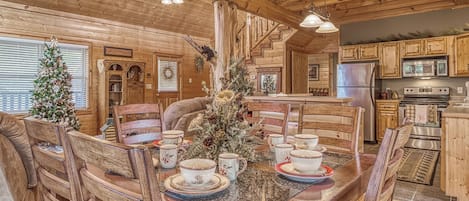 Interior de una cabaña de madera con una mesa de comedor dispuesta para cuatro personas, rodeada de sillas de madera.