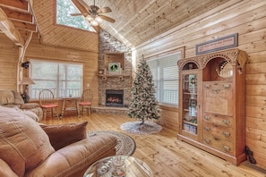A cozy log cabin interior with a fireplace, a Christmas tree, a large wooden cabinet, and a leather sofa. - Luxury! 2 Master Suites w/Fireplaces|Game Room (SEVIERVILLE)