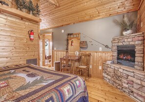 A log cabin interior with a quilted bedspread, a stone fireplace, wooden walls, and a dining area with chairs and a table. - Luxury! 2 Master Suites w/Fireplaces|Game Room (SEVIERVILLE)