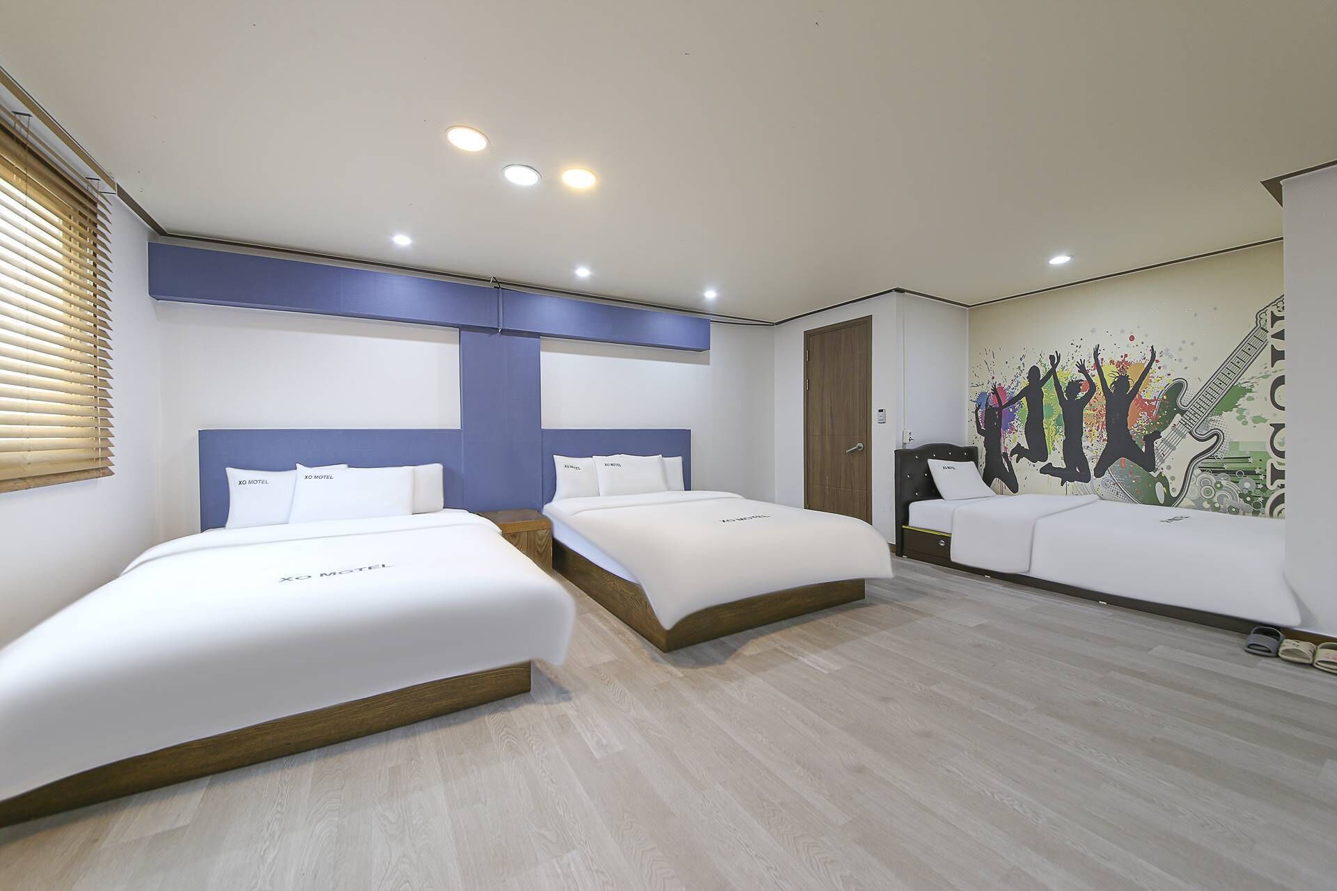 A hotel room with two single beds, a large bed, and a mural on the wall.